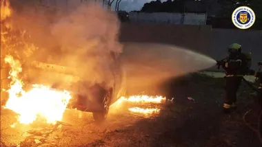 Bombero apagando vehículo envuelto en llamas.