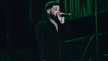 JC Reyes de negro en un concierto, sostiene el micro en su mano.