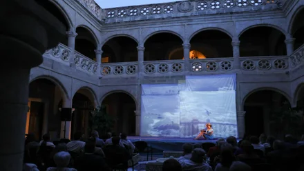 Escenario en el patio con una pantalla y una mujer leyendo poesía en la noche.