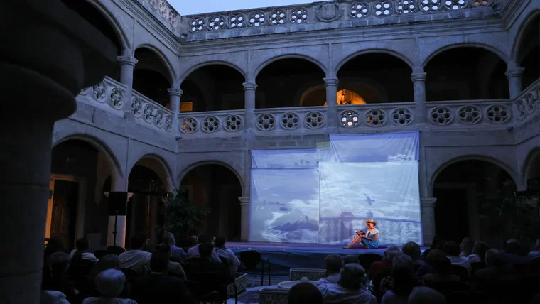 Escenario en el patio con una pantalla y una mujer leyendo poesía en la noche.