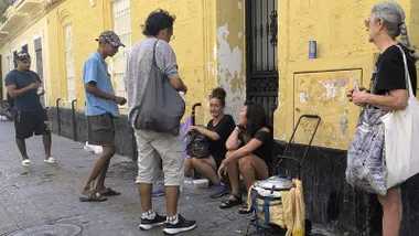 María Bonilla, embarazada de seis meses, de pie durante un reparto vecinal en la calle María Arteaga, junto a otras personas sin hogar y voluntarias que sirven comida.