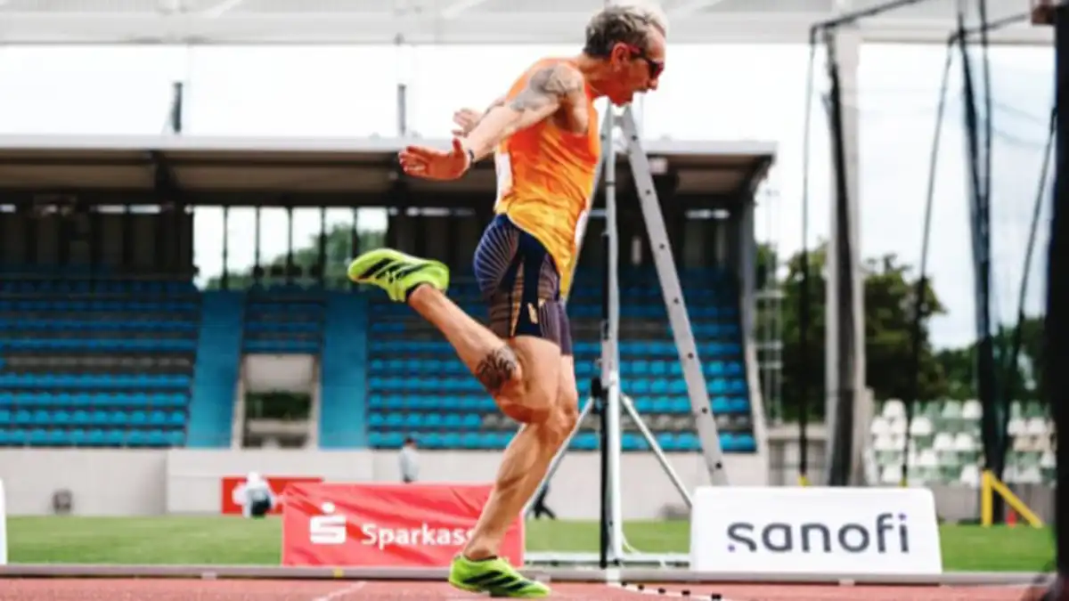 El atleta gaditano Miguel Ángel Muñoz cruza la línea de meta en Dresde durante una de las finales de los Juegos Mundiales de Trasplantados. Viste camiseta roja de España y muestra esfuerzo en el rostro mientras asegura una de las tres medallas que logró en la competición.