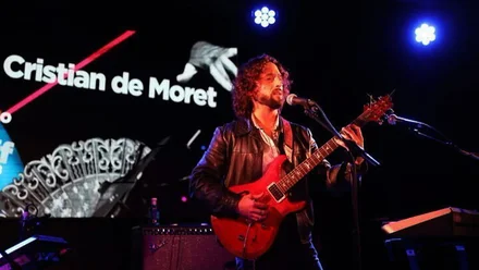 Cristian de Moret con su guitarra en el escenario, tras él un cartel luminoso con su nombre.