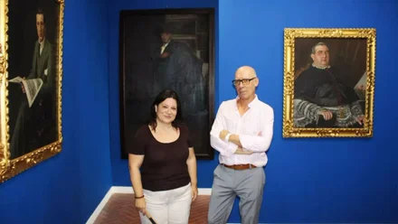 Susana Rivas, de negro, y Jesús Romero, de blanco, posando delante de unos cuadros con fondo de pared azul.