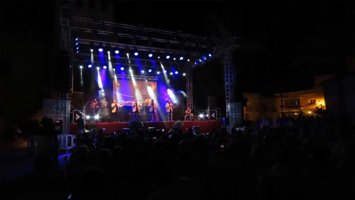 Grupo tocando en un escenario al aire libre en Rota, destacan las luces de tonos azulados.