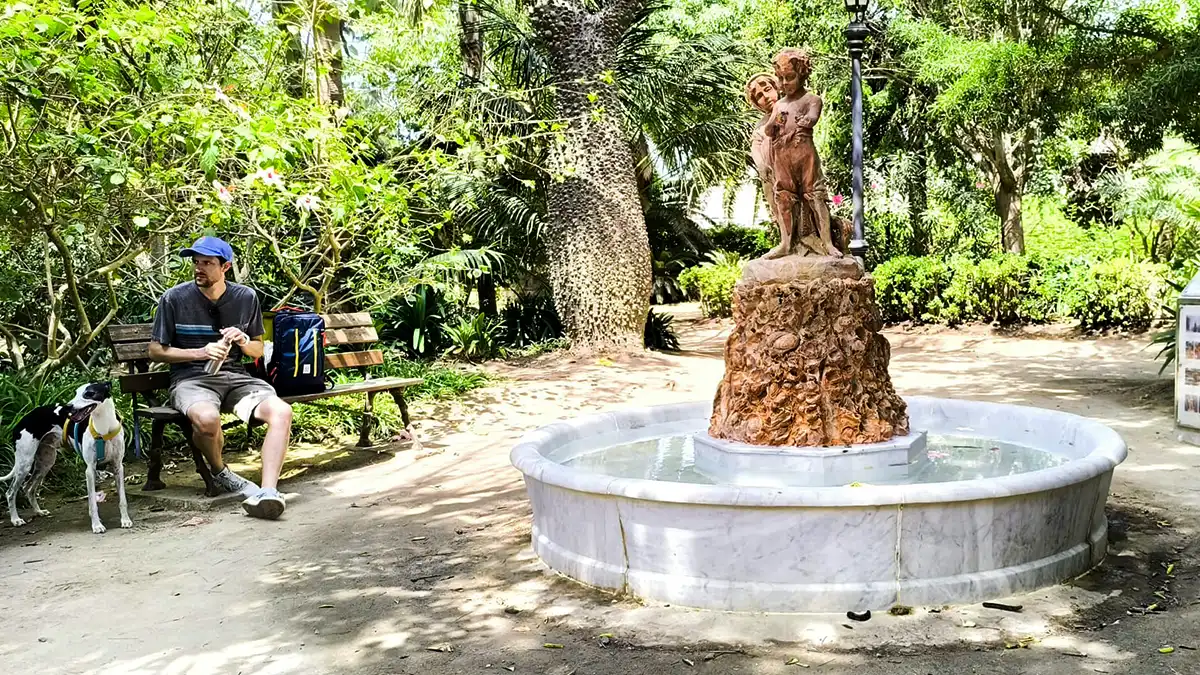Escultura de los Niños del Paraguas en el Parque Genovés, en banco a la izquierda un hombre y un perro