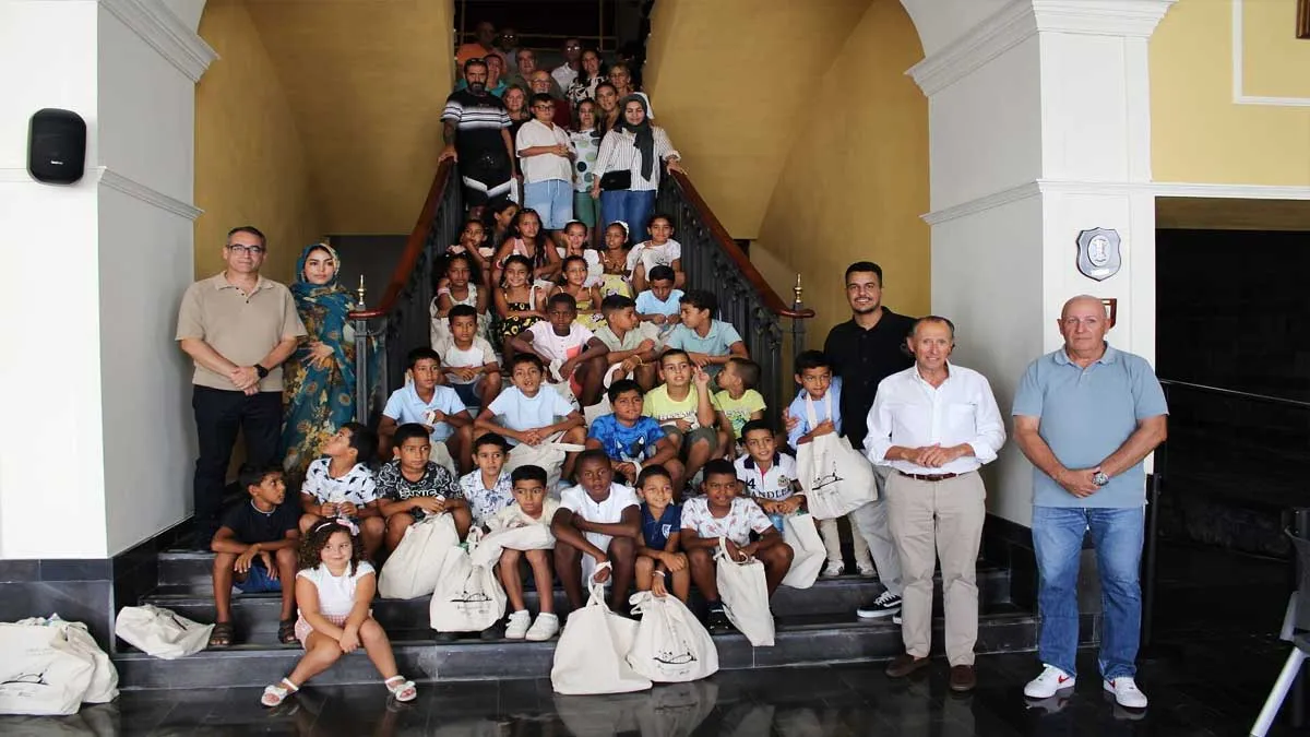 Niños sentados en las escaleras del Ayuntamiento de Chiclana, a un lado el alcalde, con camisa blanca, José María Román.