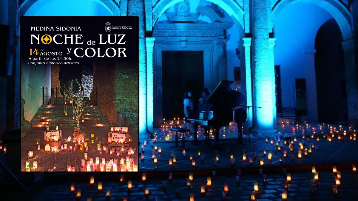 Plaza adornada con velas y un piano en medio, a la izquierda el cartel de la "Noche de Luz y Color" de Medina Sidonia.