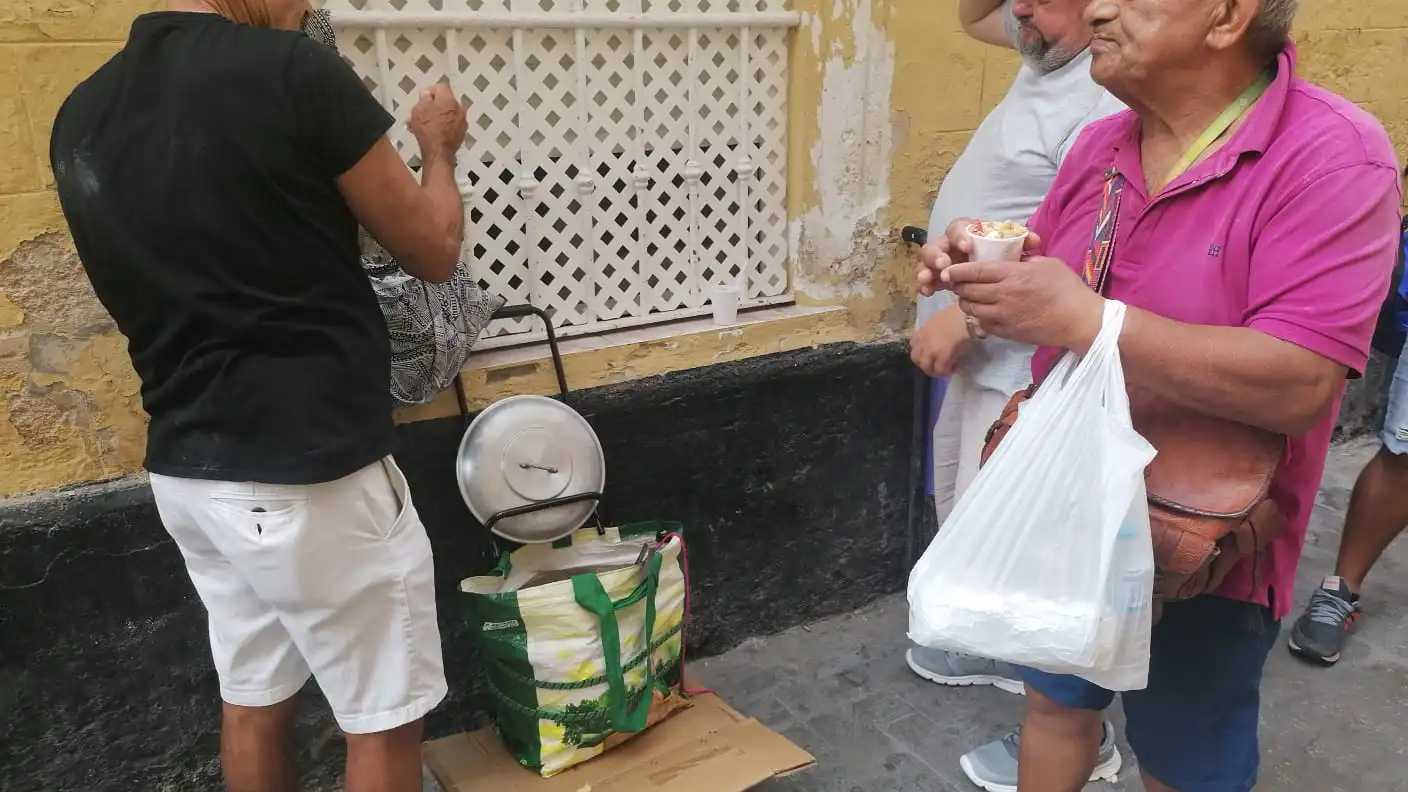 Dos personas reciben papás aliñás en un momento del un momento del reparto solidario organizado por vecinos de Cádiz tras el cierre de comedores sociales.