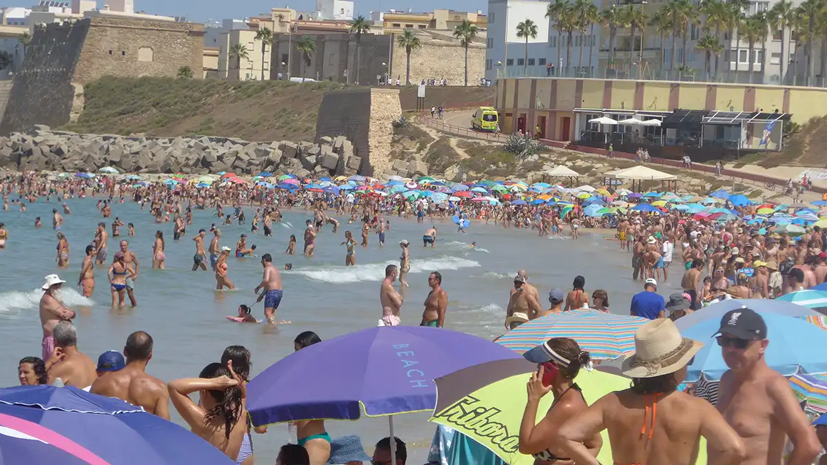 Playa de Santa María del Mar en Cádiz abarrotada de bañistas bajo sombrillas de colores. El mar en calma y el cielo despejado completan la imagen de un día de calor sofocante en la ciudad.