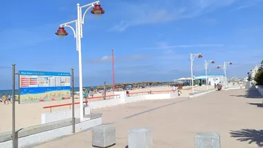 Fotografía tomada desde el paseo marítimo de Cádiz, donde se observa la playa de la Victoria con el mar en calma, arena clara y un cielo completamente azul y despejado.
