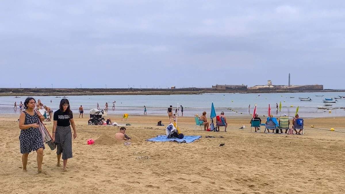 Fotografía de la playa de La Caleta en Cádiz tomada a primera hora del domingo 24 de agosto. El cielo está completamente cubierto de nubes y el ambiente transmite humedad por el viento fresco del suroeste. Varias personas se marchan de la orilla mientras un hombre permanece en la arena excavando un gran boquete