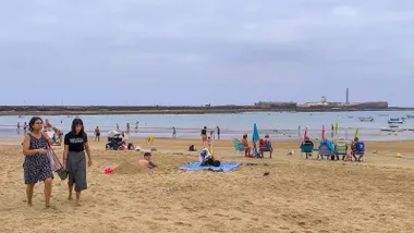 Fotografía de la playa de La Caleta en Cádiz tomada a primera hora del domingo 24 de agosto. El cielo está completamente cubierto de nubes y el ambiente transmite humedad por el viento fresco del suroeste. Varias personas se marchan de la orilla mientras un hombre permanece en la arena excavando un gran boquete
