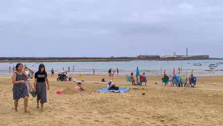 Fotografía de la playa de La Caleta en Cádiz tomada a primera hora del domingo 24 de agosto. El cielo está completamente cubierto de nubes y el ambiente transmite humedad por el viento fresco del suroeste. Varias personas se marchan de la orilla mientras un hombre permanece en la arena excavando un gran boquete