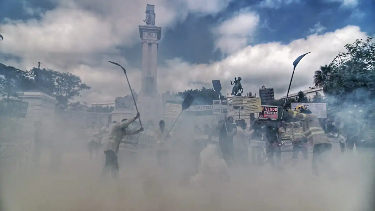 Manifestación de bomberos forestales del Plan Infoca en la Plaza de España de Cádiz. Se ven pancartas con lemas como “Se vende Infoca” y humo de colores frente al monumento de la Constitución de 1812.
