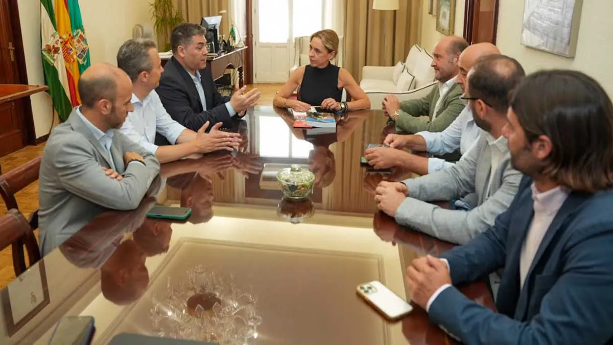 Martínez, con blusa negra, sentada en una mesa con los representantes que la miran.