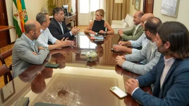 Martínez, con blusa negra, sentada en una mesa con los representantes que la miran.