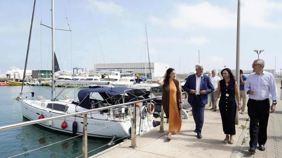 Consejera de la Junta de Andalucía, junto a otras personalidades, en el puerto de Chipiona, están en el muelle y hay barcos.