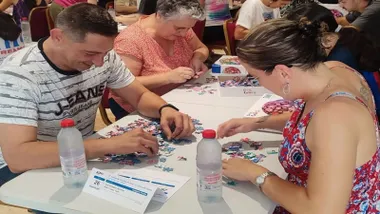 Hombre y mujer realizando un puzle sobre una mesa, ambos sonríen.