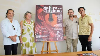 Martínez Rico, con vestido claro estampado, junto al cartel de "Salero en Chiclana" y los organizadores.