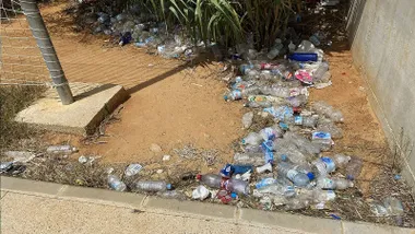 Suciedad, con botellas y latas tiradas en el suelo, en El Puerto, sobre un terreno de arena.
