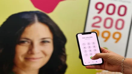 Mano pulsando el teclado de un teléfono contra la violencia sexual, con un rostro de fondo y el número 900 200 999.