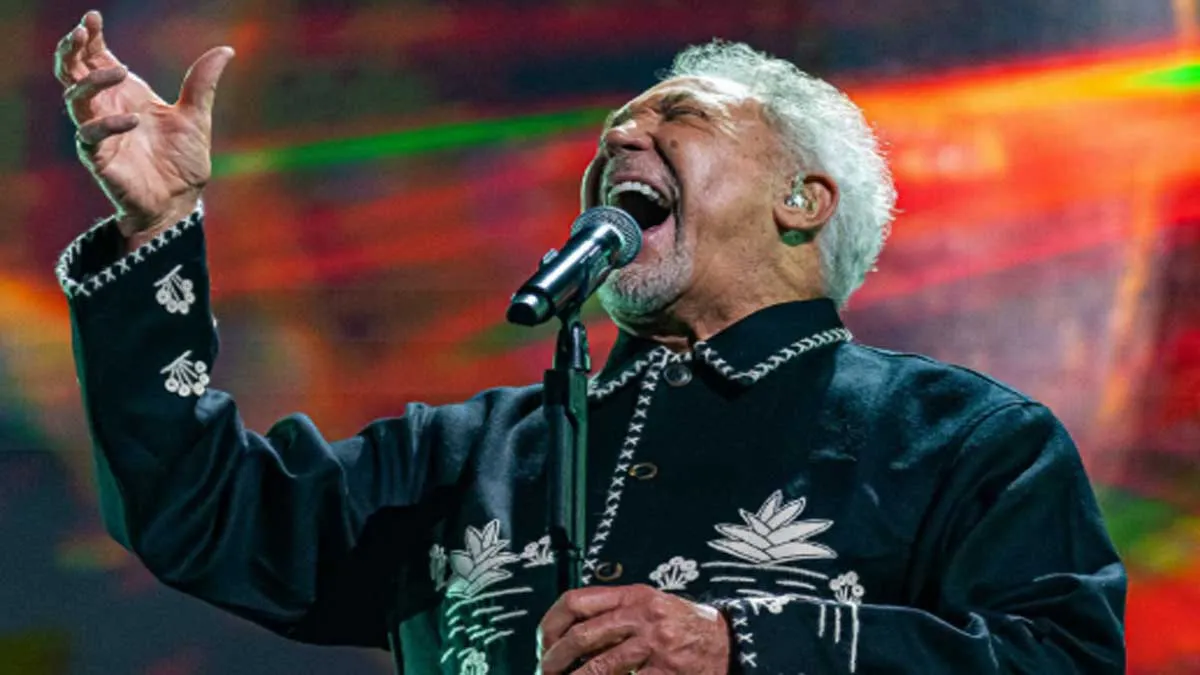 Tom Jones, con camisa negra y adornos blancos mientras canta.