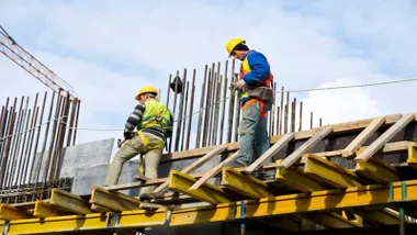 Dos trabajadores con casco en un andamio.