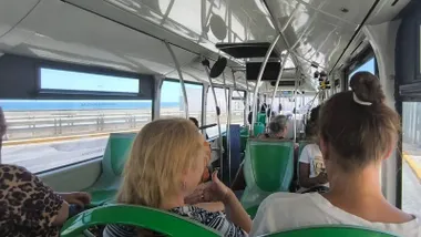 Pasajeros sentados dentro de un autobús urbano se abanican con la mano para aliviar el calor; la luz del sol entra por las ventanillas.