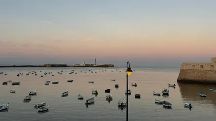 Imagen casi de postal de La Caleta de Cádiz a primera hora de la mañana, con el mar en calma, las barquitas y los dos castillos.
