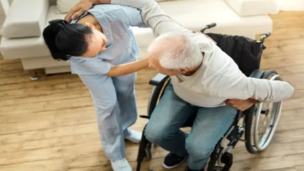 Asistente de ayuda a domicilio levanta a un hombre en silla de ruedas.