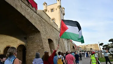 Una mujer ondea una bandera de Palestina al pasar por la Puerta de Tierra en la cadena humana de este lunes en Cádiz.