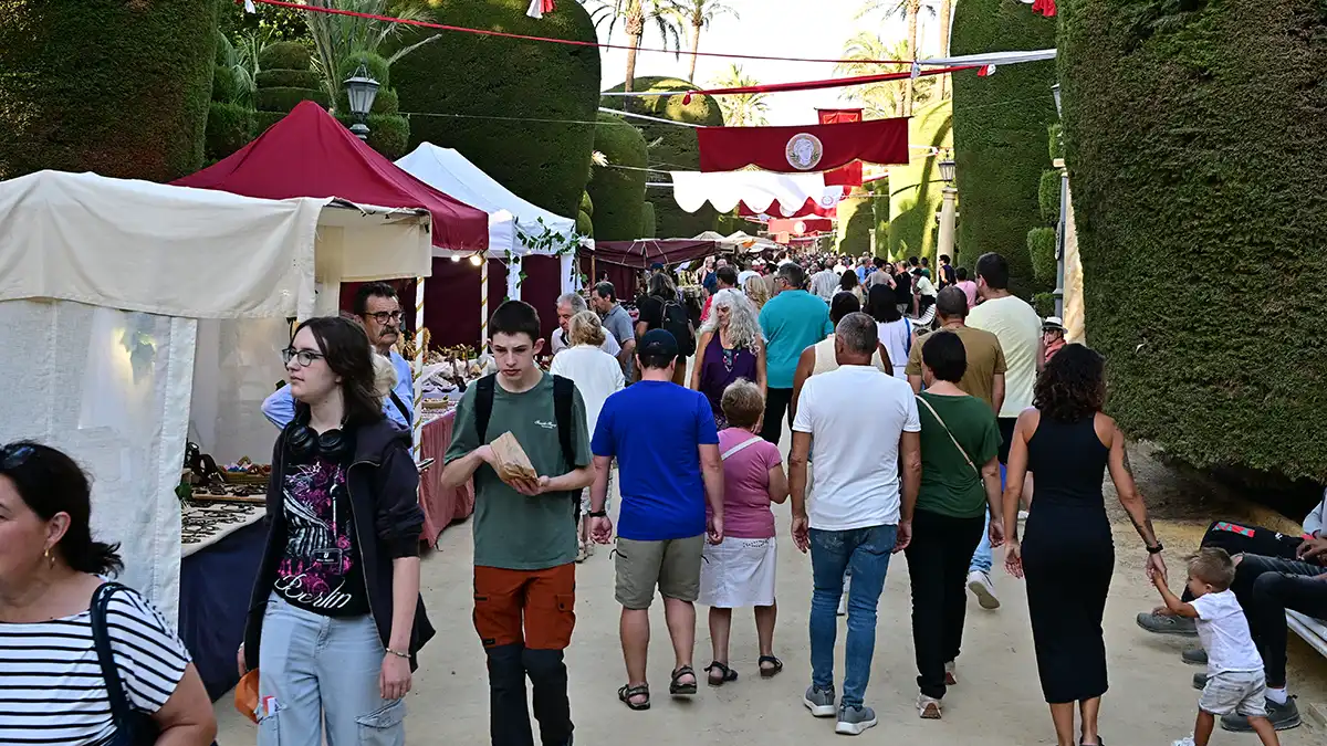 Multitud de visitantes paseando entre los puestos de madera decorados con estandartes romanos.