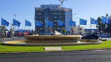 Varias banderas de la Regata Globe 40 ondean en la Plaza de Sevilla de Cádiz. La imagen muestra el ambiente previo a la llegada de los barcos, con colores vivos y el entorno urbano decorado para el evento.