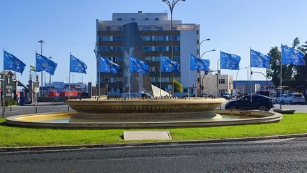 Varias banderas de la Regata Globe 40 ondean en la Plaza de Sevilla de Cádiz. La imagen muestra el ambiente previo a la llegada de los barcos, con colores vivos y el entorno urbano decorado para el evento.