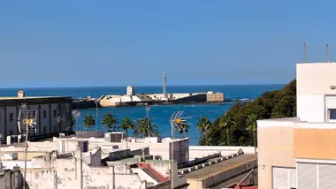 Vista del cielo despejado sobre la playa de La Caleta en Cádiz, con el castillo de San Sebastián al fondo, tomada desde una azotea del barrio de La Viña.
