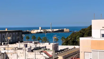 Vista del cielo despejado sobre la playa de La Caleta en Cádiz, con el castillo de San Sebastián al fondo, tomada desde una azotea del barrio de La Viña.