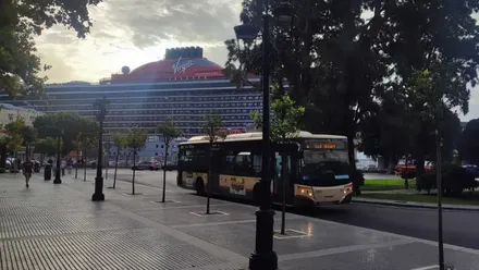 Un crucero atracado en el muelle de Cádiz en un dñia nuboso visto desde la Plaza de España a cuya parada llega un autobús urbano