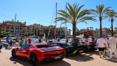 Diferentes vehículos de alta gama, uno rojo y dos negros en la exposición al aire libre en Puerto Sotogrande.