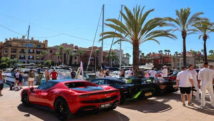 Diferentes vehículos de alta gama, uno rojo y dos negros en la exposición al aire libre en Puerto Sotogrande.