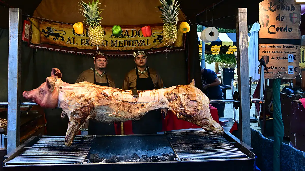 Pieza entera de cochinillo expuesta en un asador al aire libre. Al estilo medieval, dice en el cartel de atrás.