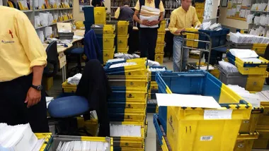 Carteros clasificando muchas cartas y paquetes acumulados en una estafeta.