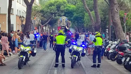 Dos agentes de la Policía Local de Cádiz con chalecos reflectantes cortan una calle del centro histórico mientras peatones y público observan durante el desfile inaugural de Cádiz Romana.