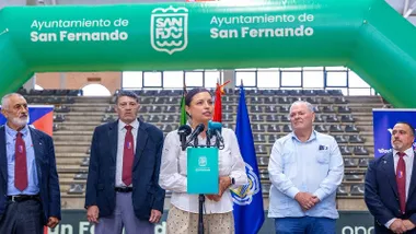 La alcaldesa de San Fernando con los organizadores tras ella y un pórtico en verde y blanco de la localidad.