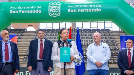 La alcaldesa de San Fernando con los organizadores tras ella y un pórtico en verde y blanco de la localidad.