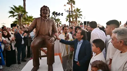 Juanito Villar, de perfil y visiblemente emocionado, observa su escultura recién inaugurada en la plaza Canal de Ponce, con el entorno de La Caleta de fondo.