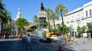 Vista de la estatua de bronce de Segismundo Moret en la plaza de San Juan de Dios, rodeada por vallas de protección y una plataforma elevadora junto al monumento para los trabajos de limpieza.