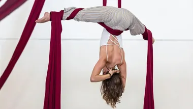 Chica colgada de telas color burdeos en acrobacias aéreas.