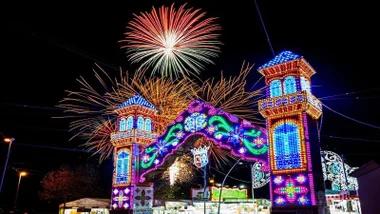 Portada iluminada en muchos colores en la Feria de Conil y fuegos artificiales tras ella.