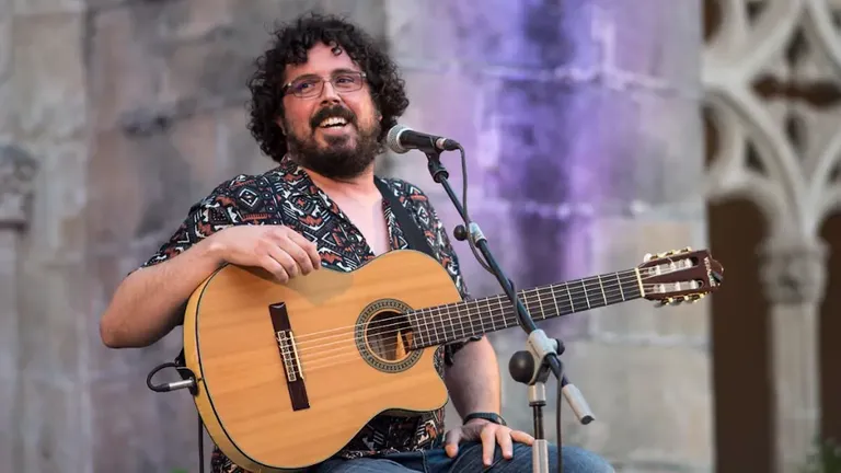 Fernando Lobo sentado con camisa estampada y su inseparable guitarra.